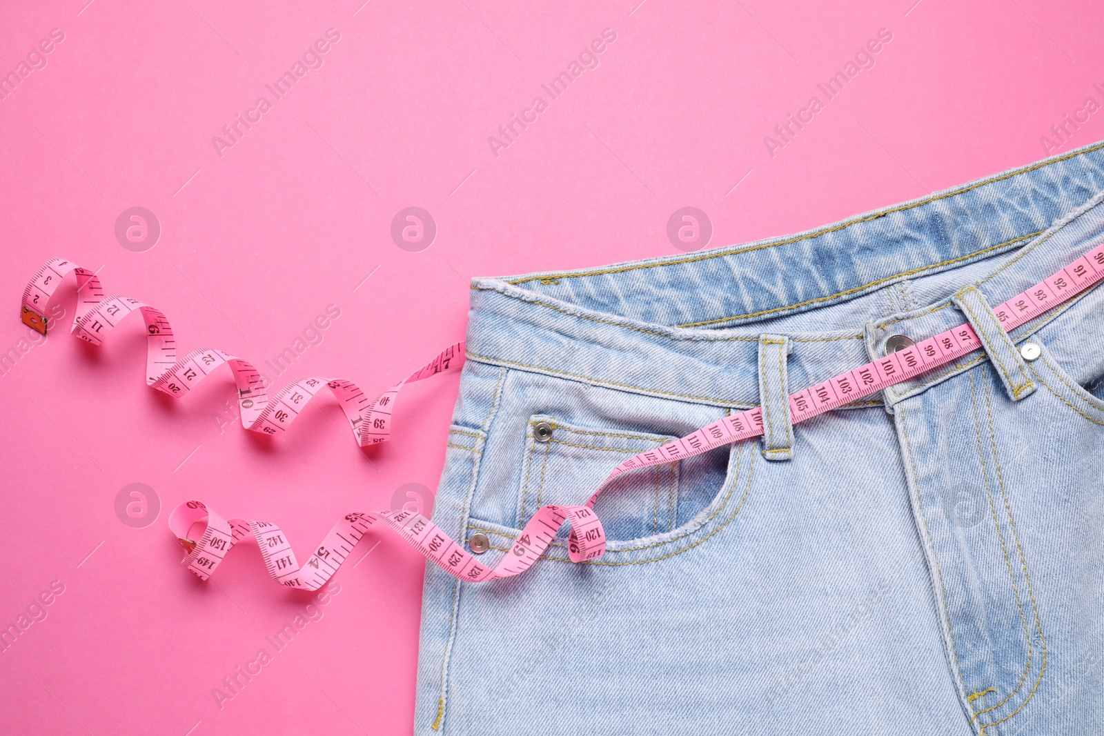 Photo of Jeans and measuring tape on pink background, top view