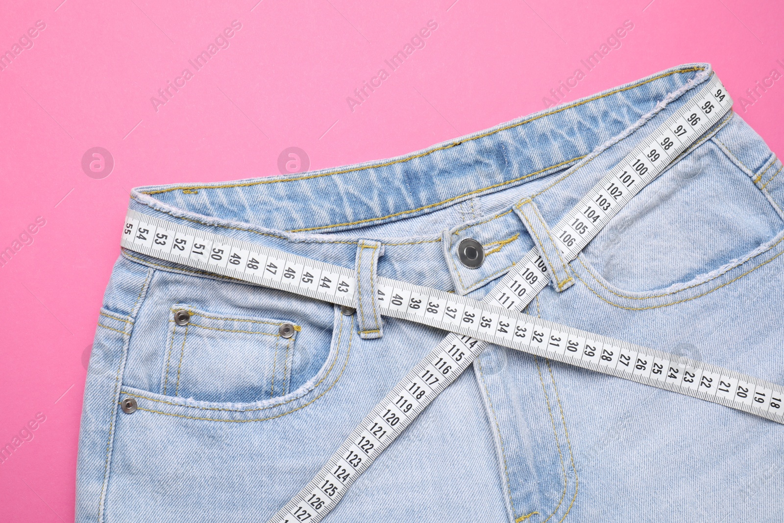 Photo of Jeans and measuring tape on pink background, top view