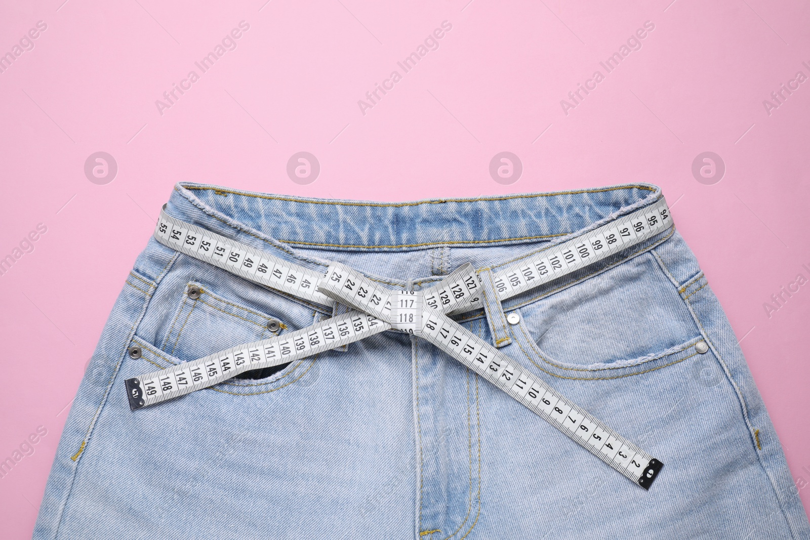 Photo of Jeans and measuring tape on pink background, top view