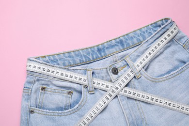 Photo of Jeans and measuring tape on pink background, top view