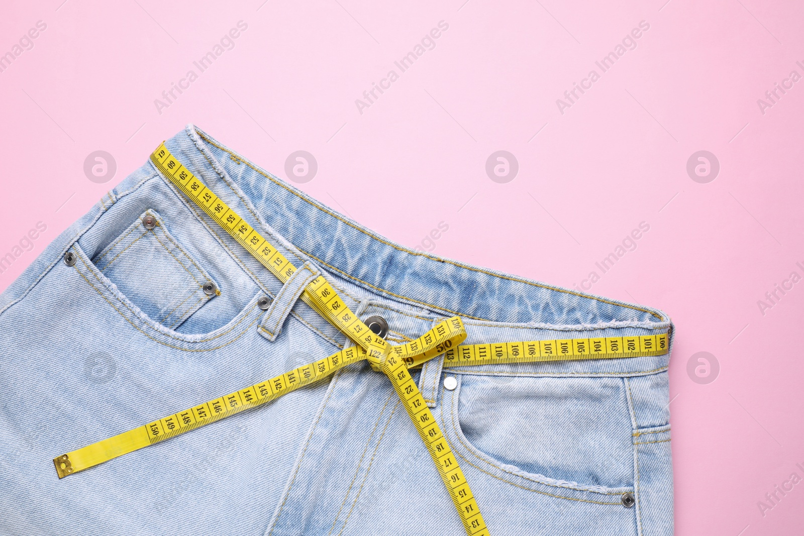 Photo of Jeans and measuring tape on pink background, top view