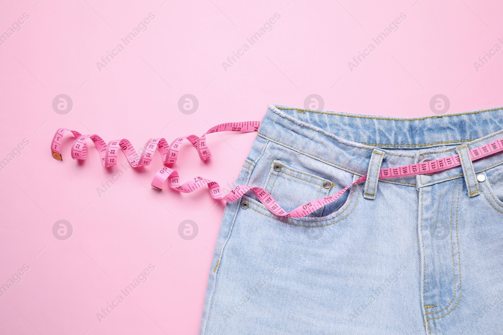 Photo of Jeans and measuring tape on pink background, top view