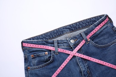 Photo of Jeans and measuring tape on white background, top view