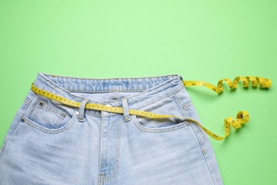 Photo of Jeans and measuring tape on green background, top view