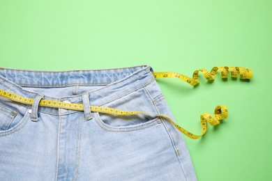 Photo of Jeans and measuring tape on green background, top view