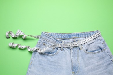 Photo of Jeans and measuring tape on green background, top view