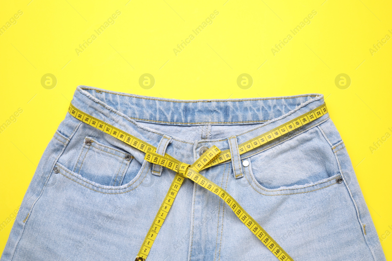 Photo of Jeans and measuring tape on yellow background, top view