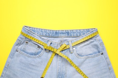 Photo of Jeans and measuring tape on yellow background, top view