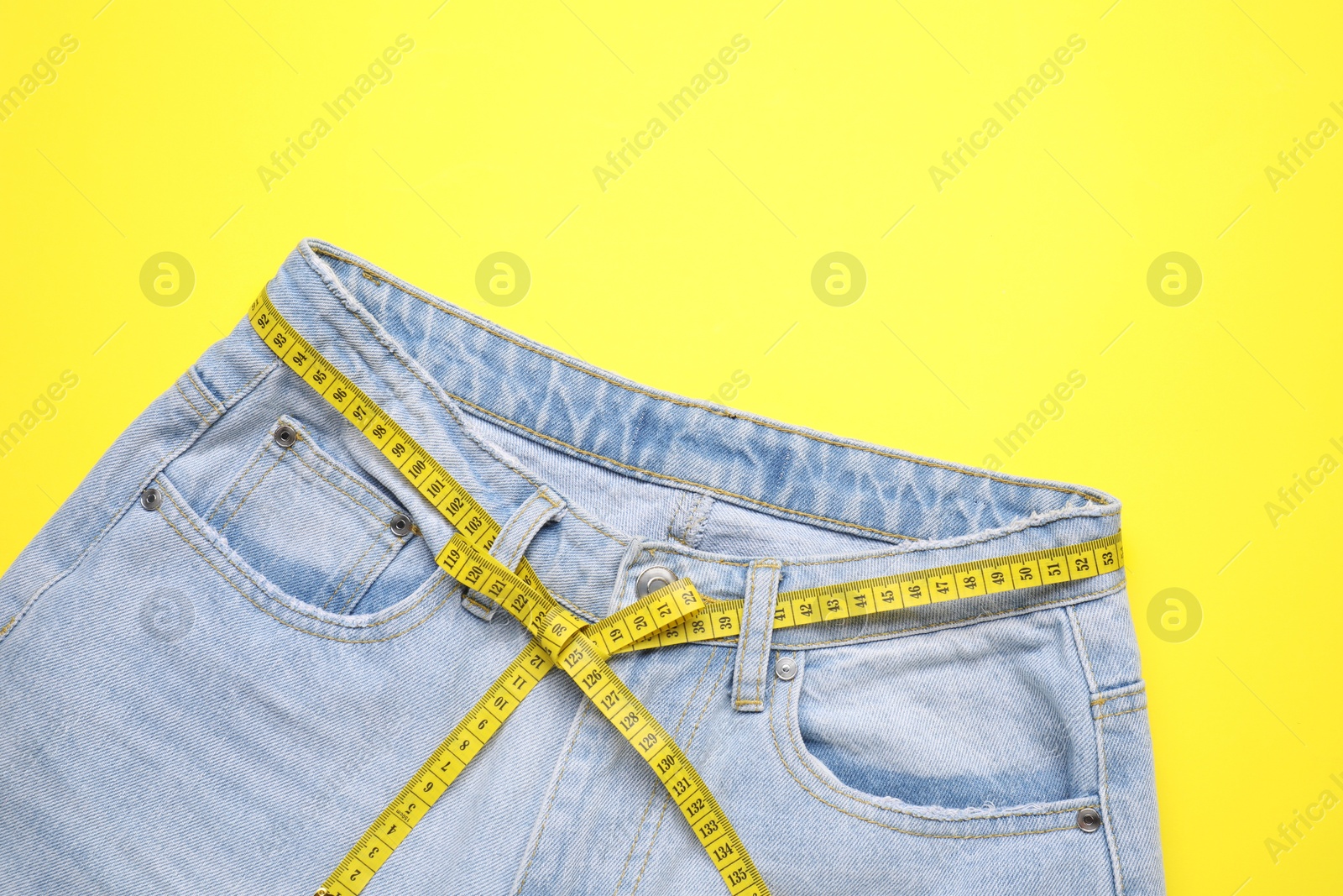 Photo of Jeans and measuring tape on yellow background, top view