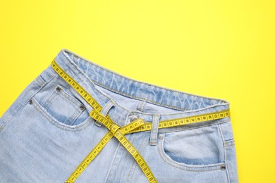 Photo of Jeans and measuring tape on yellow background, top view