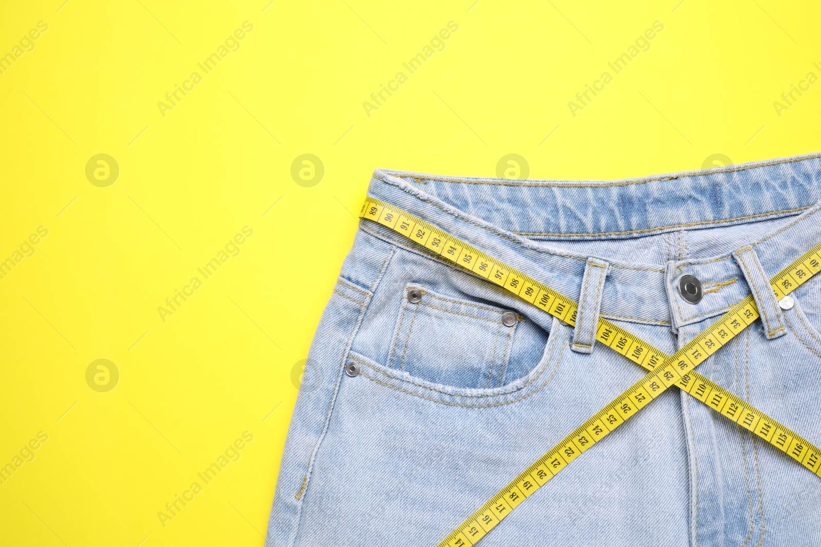 Photo of Jeans and measuring tape on yellow background, top view. Space for text