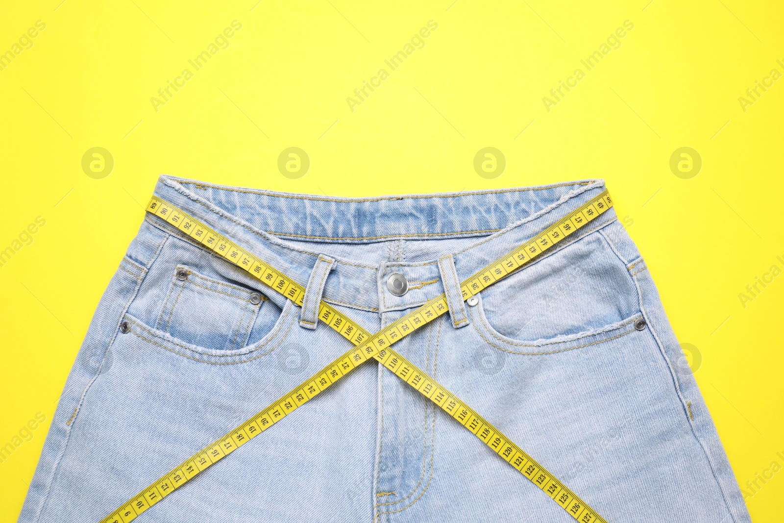 Photo of Jeans and measuring tape on yellow background, top view