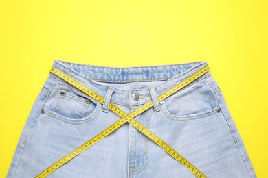 Photo of Jeans and measuring tape on yellow background, top view