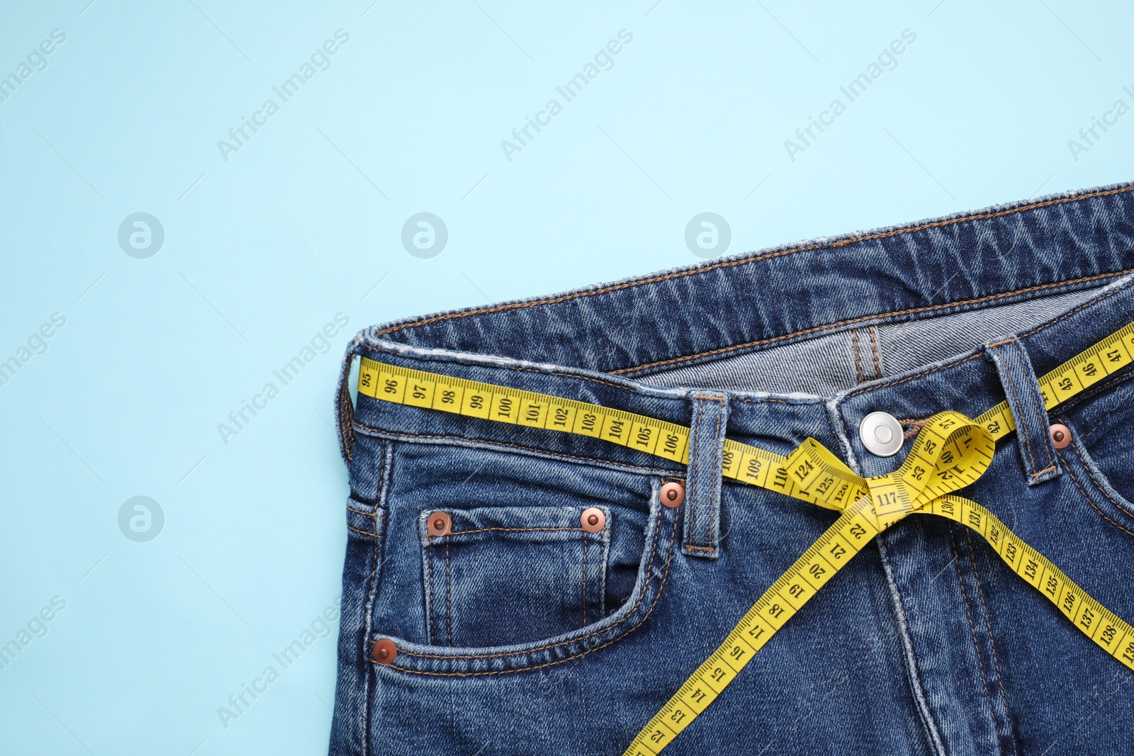 Photo of Jeans and measuring tape on light blue background, top view. Space for text