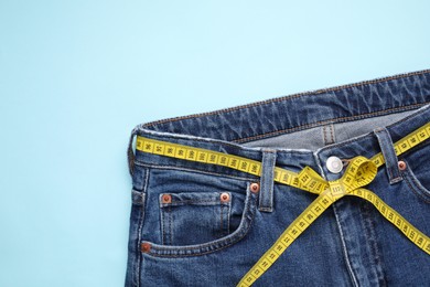 Photo of Jeans and measuring tape on light blue background, top view. Space for text