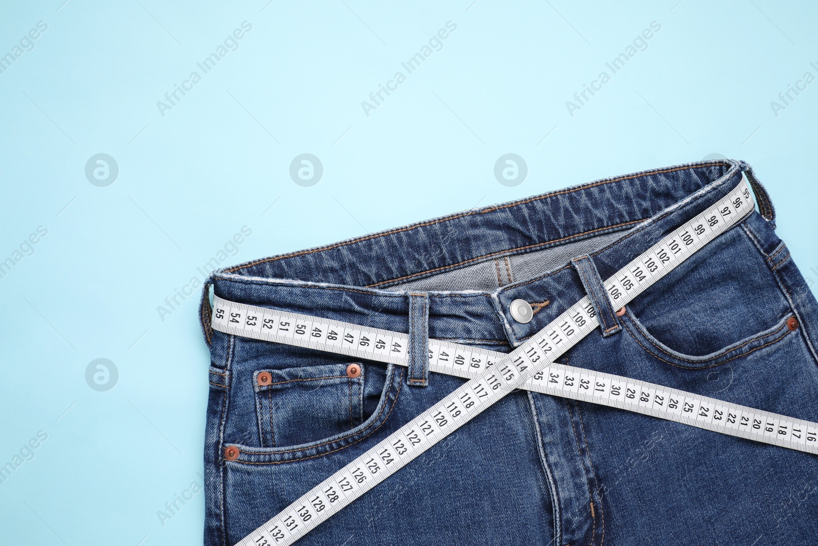 Photo of Jeans and measuring tape on light blue background, top view. Space for text