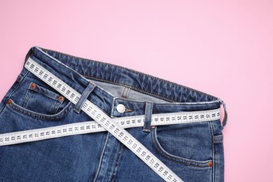 Photo of Jeans and measuring tape on pink background, top view. Space for text