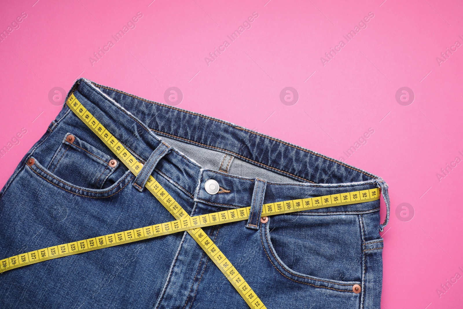 Photo of Jeans and measuring tape on pink background, top view