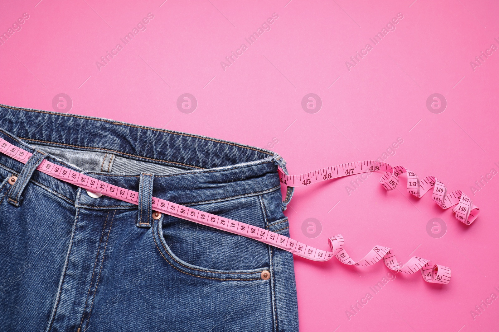 Photo of Jeans and measuring tape on pink background, top view