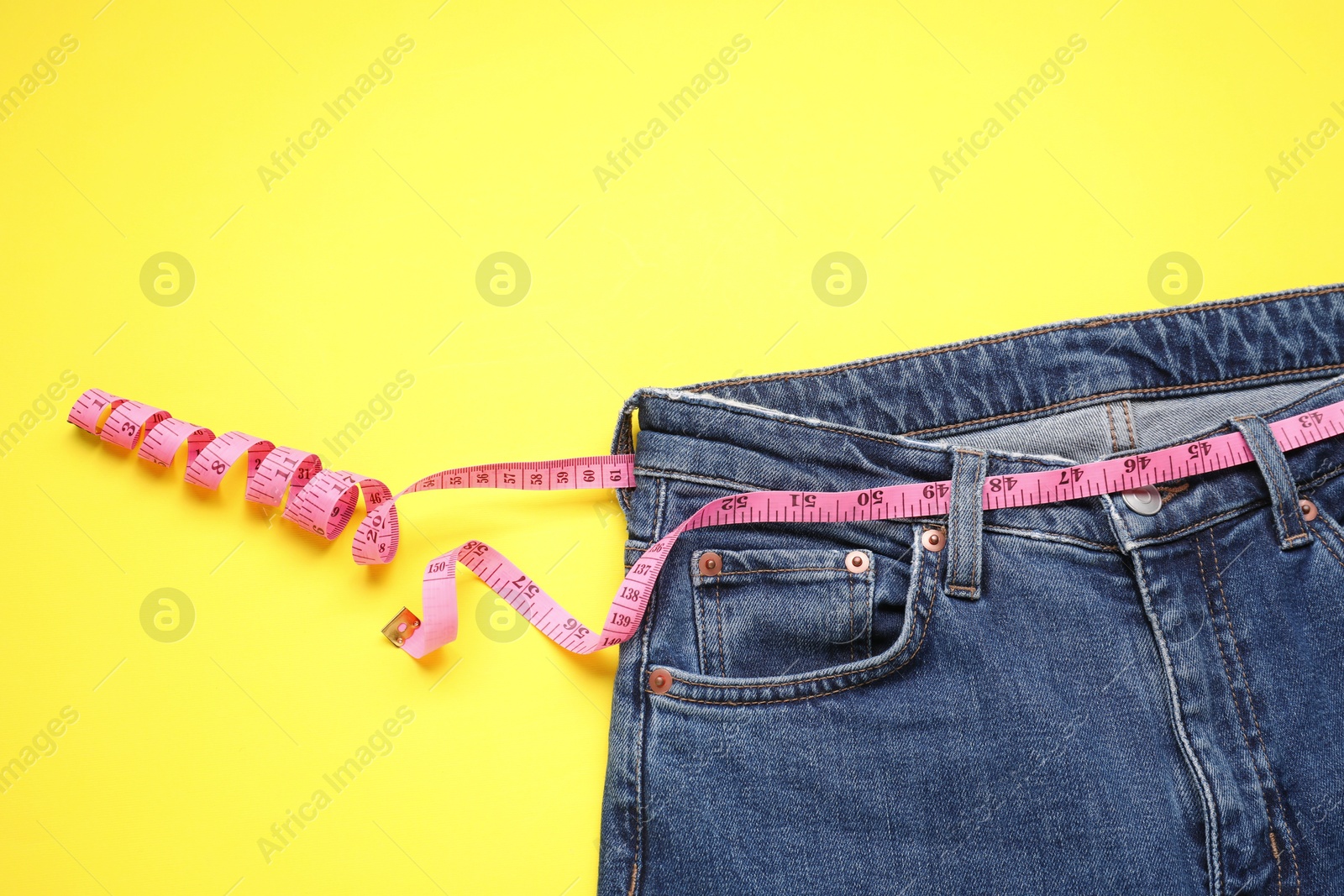 Photo of Jeans and measuring tape on yellow background, top view. Space for text