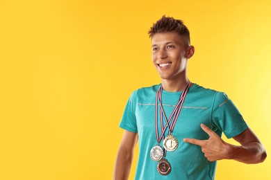 Photo of Happy winner pointing at his medals on yellow background. Space for text