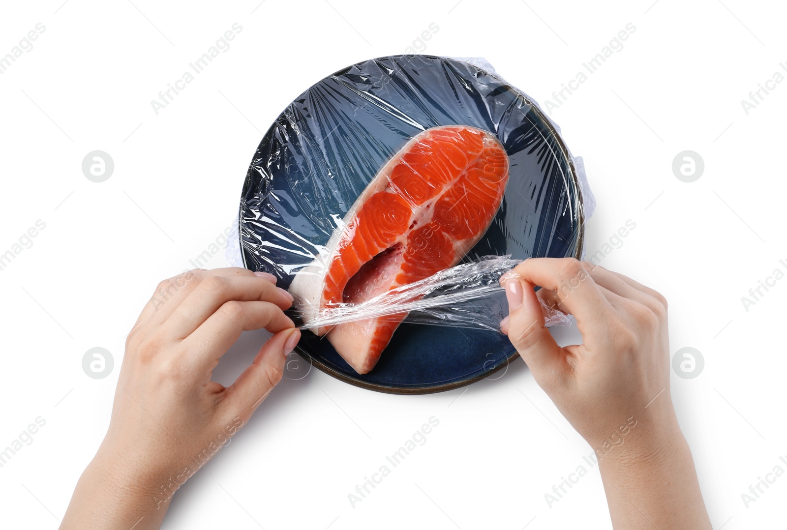 Photo of Woman putting plastic food wrap over plate with salmon on white background, top view