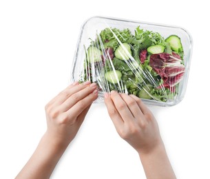 Woman putting plastic food wrap over glass container with fresh salad on white background, top view