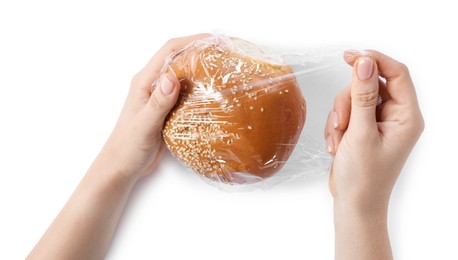 Woman putting plastic food wrap over fresh bun on white background, top view