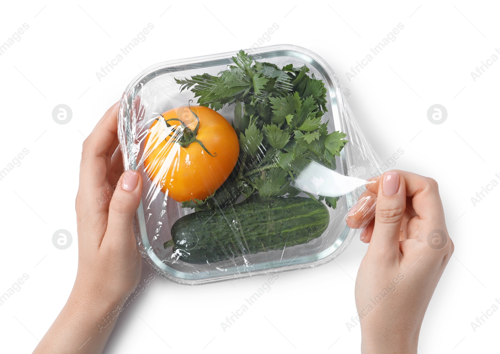 Photo of Woman putting plastic food wrap over glass container with vegetables on white background, top view