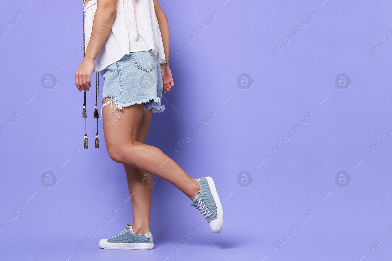 Photo of Woman wearing stylish denim shorts on violet background, closeup. Space for text