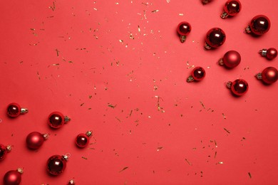 Photo of Christmas balls and confetti on red background, flat lay. Space for text