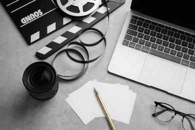 Camera lens, movie clapper and laptop on grey textured table, above view