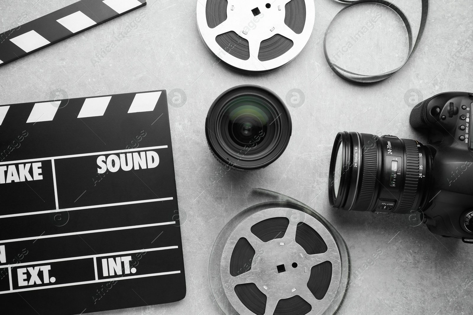 Photo of Movie clapper, film reels and camera on grey textured table, flat lay