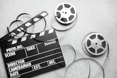 Movie clapper and film reels on grey textured table, flat lay