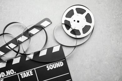 Photo of Movie clapper and film reel on grey textured table, flat lay