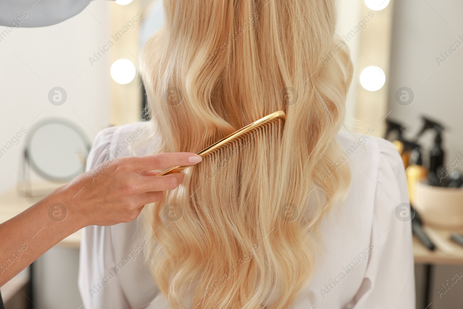 Photo of Professional hairdresser combing woman's hair in salon, closeup