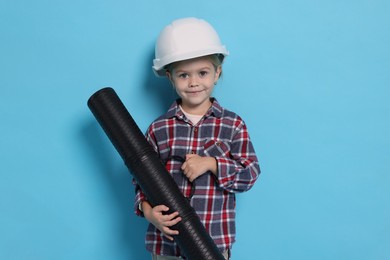 Photo of Little girl with blueprint tube pretending to be architect on light blue background. Dreaming of future profession