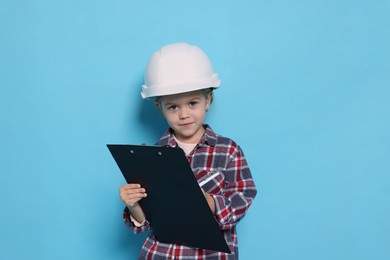 Little girl with clipboard pretending to be architect on light blue background. Dreaming of future profession