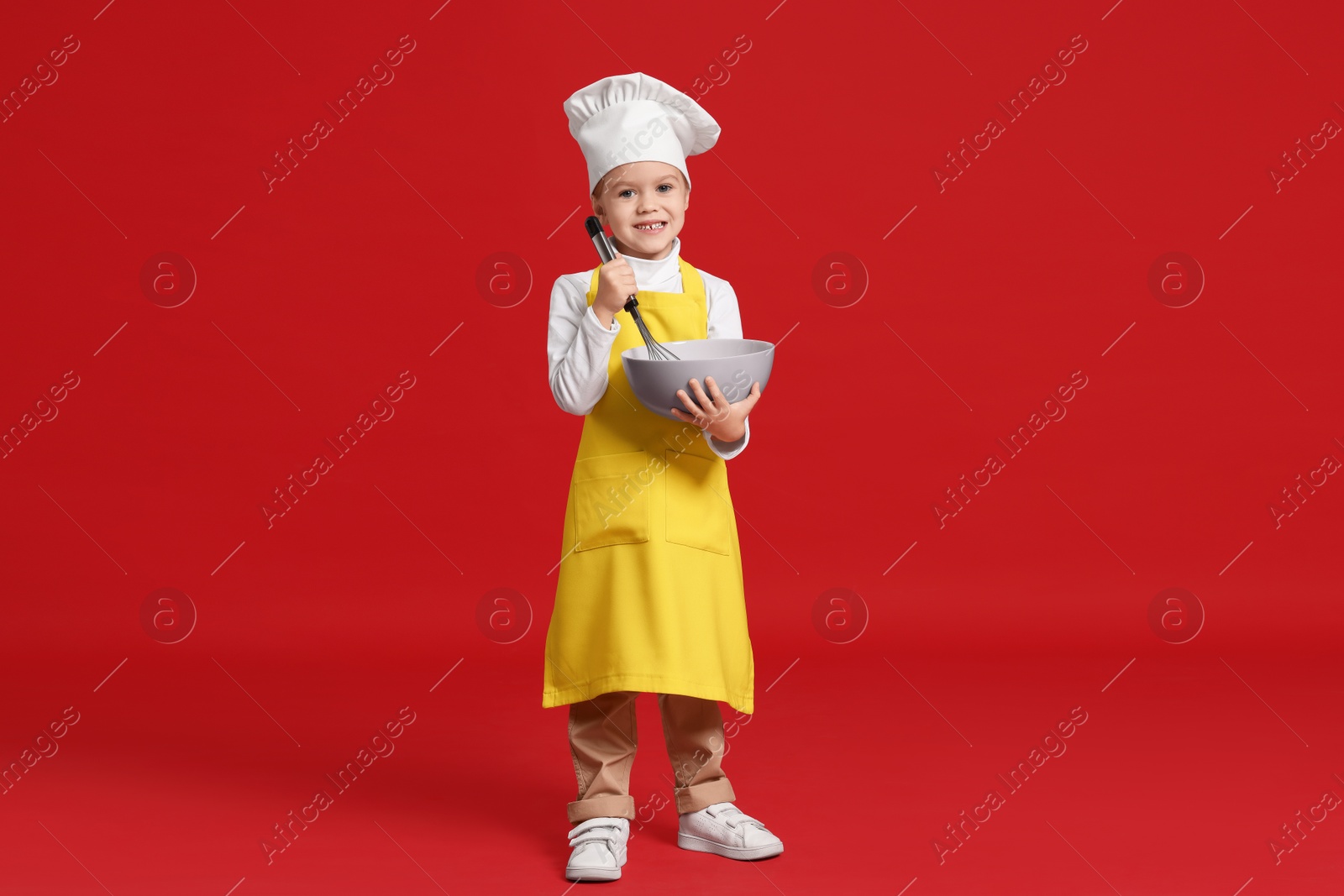 Photo of Little girl with bowl and whisk pretending to be chef on red background. Dreaming of future profession