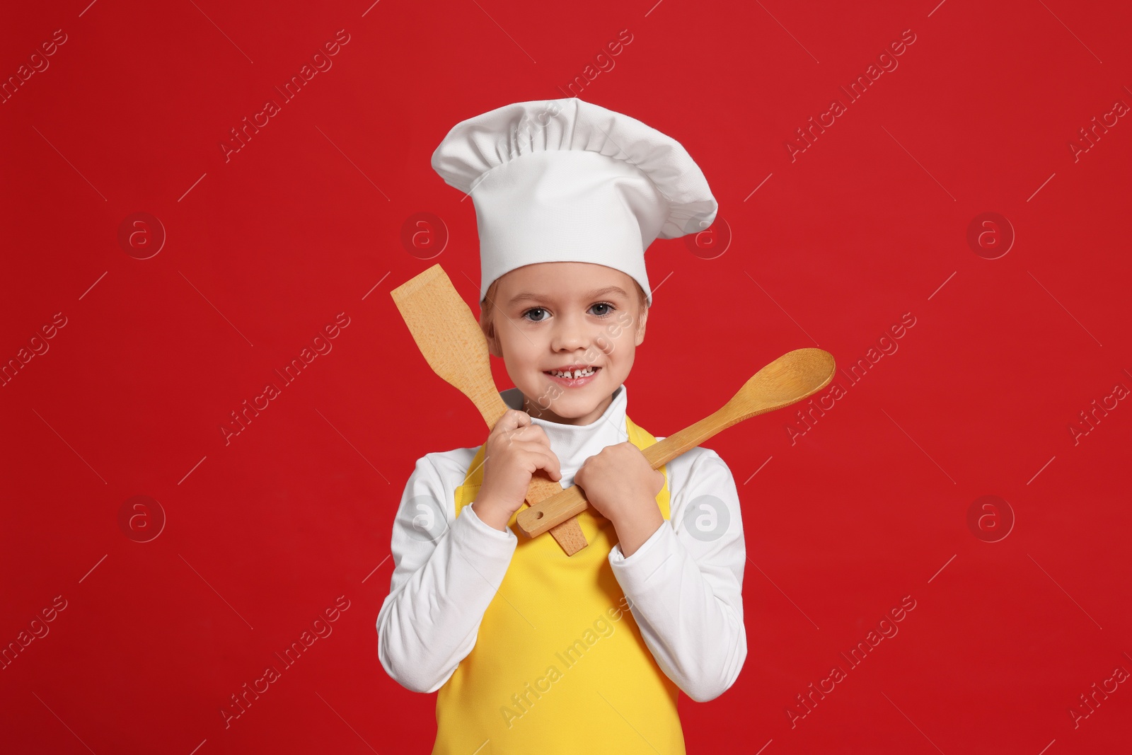 Photo of Little girl with utensils pretending to be chef on red background. Dreaming of future profession