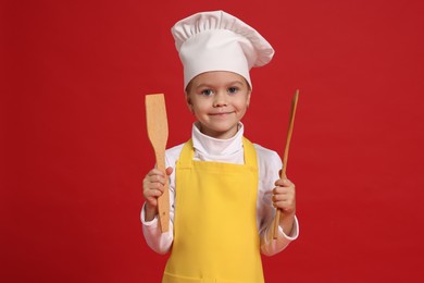 Photo of Little girl with utensils pretending to be chef on red background. Dreaming of future profession