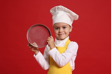 Little girl with sieve pretending to be chef on red background. Dreaming of future profession