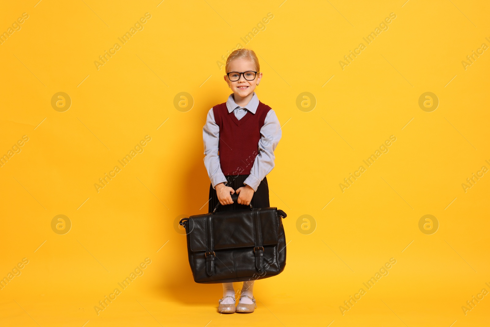 Photo of Little girl with glasses and briefcase on orange background. Dreaming of future profession