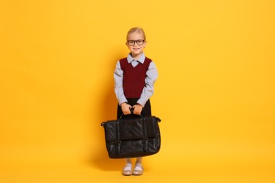 Little girl with glasses and briefcase on orange background. Dreaming of future profession