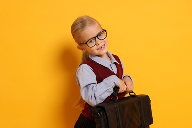 Little girl with glasses and briefcase on orange background. Dreaming of future profession