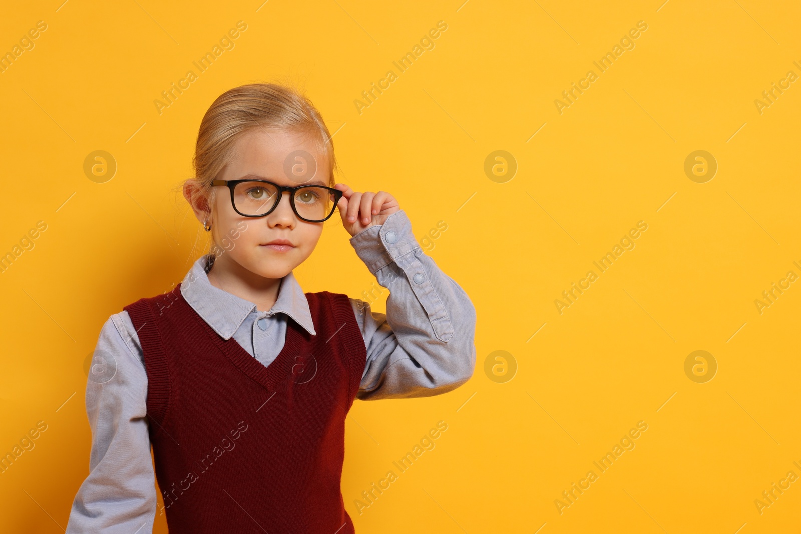 Photo of Little girl with glasses on orange background, space for text. Dreaming of future profession