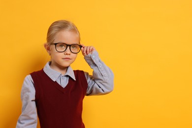 Photo of Little girl with glasses on orange background, space for text. Dreaming of future profession