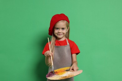 Photo of Little girl with brush and palette pretending to be artist on green background. Dreaming of future profession