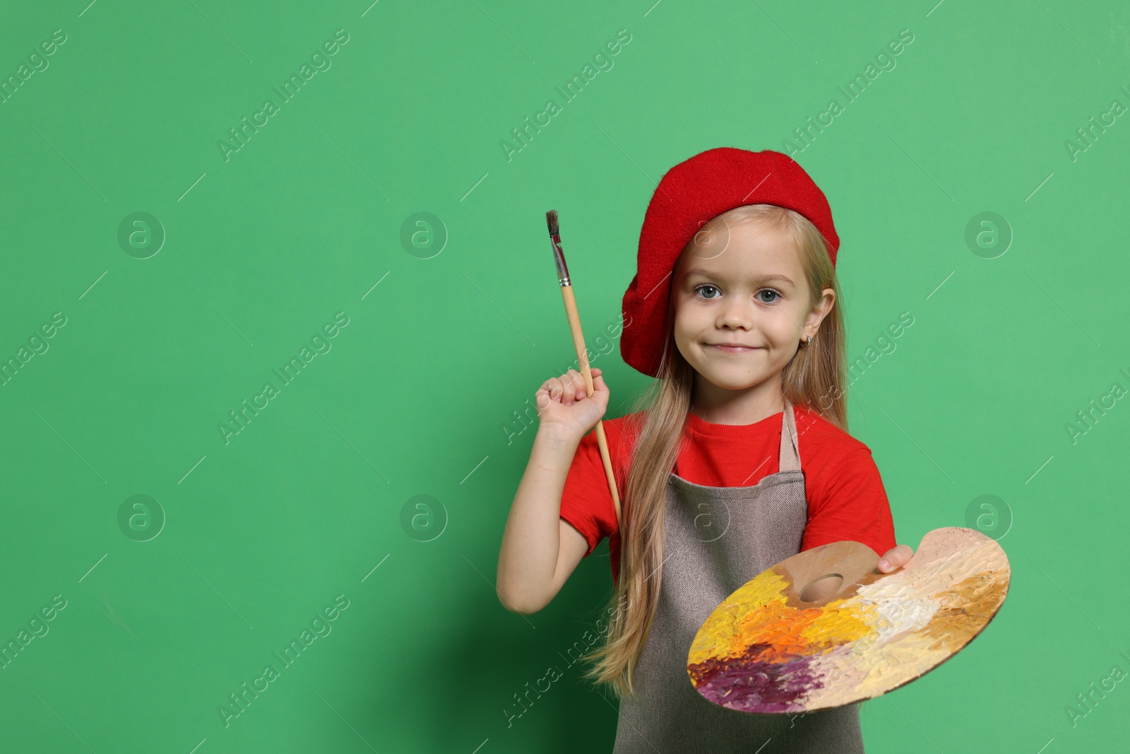 Photo of Little girl with brush and palette pretending to be artist on green background. Dreaming of future profession