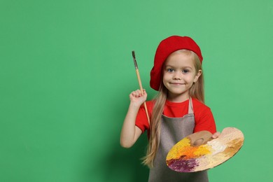 Photo of Little girl with brush and palette pretending to be artist on green background. Dreaming of future profession